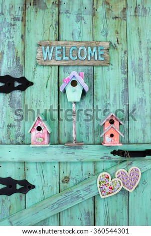 Welcome sign, birdhouses and country hearts hanging on antique mint green rustic wood door