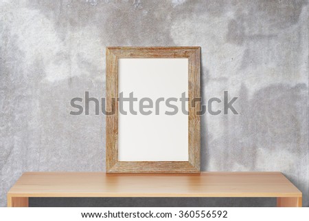 Blank wooden picture frame standing on the wooden table on a background of a concrete wall, mock up