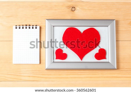 Photo frames, blank card and handmade hearts over wooden background