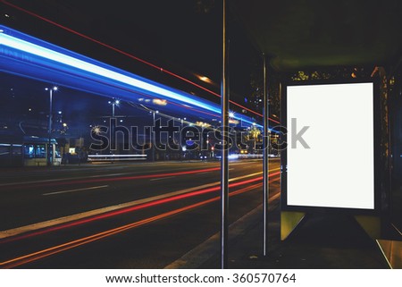 Illuminated blank billboard with copy space for your text message or promotional content, advertising mock up banner on bus stop in night, public information board with blurred vehicles on high speed