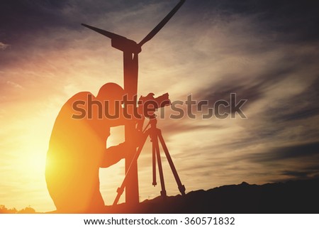 Man geo-desist using theodolite for measures distance for the construction of the new building while standing against wind turbine and sunset, male surveyor determines the required coordinates