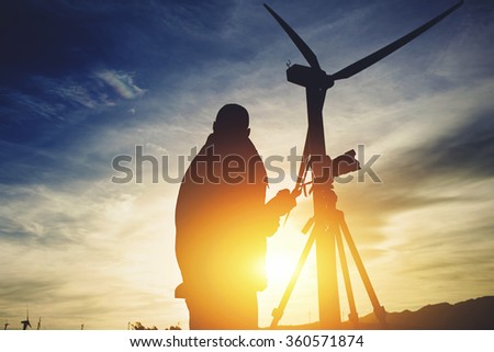 Silhouette of a male surveyor standing with theodolite against electric generator and evening sky while measuring the distance for the construction of a new highway, man geo desist working outside 