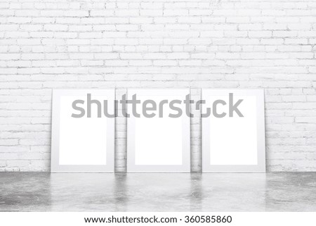 Blank white picture frames on concrete floor in empty loft room with white brick wall, mock up