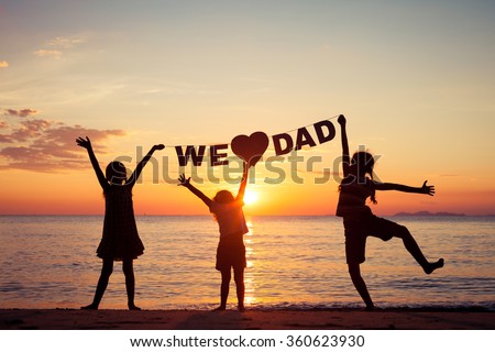 Happy children playing on the beach at the sunset time. Children hold in the hands  inscription "We love dad". Concept of happy father day.