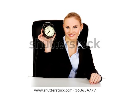 Happy business woman with alarm clock behind the desk