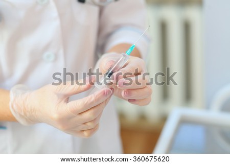 nurse in a white coat and gloved hands holding a disposable syringe with medicine