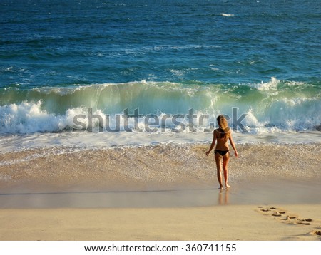 Girl in swimming suit standind at the ocean beach with wave