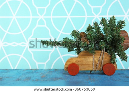 Wooden toy car with Christmas tree on a table over pattern background