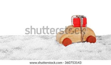 Wooden toy car with gift box on a snowy table over white background