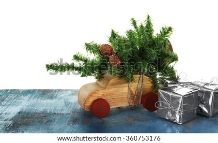 Wooden toy car with Christmas tree and gift boxes on a table over white background