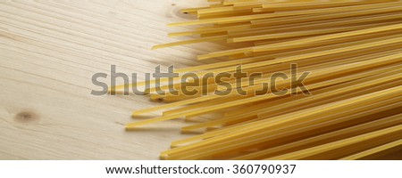 Bundle of raw uncooked Italian pasta spaghetti macaroni lying on a textured wooden surface with shallow dof and focus to the ends of the strands with space for text  - banner / header edition   