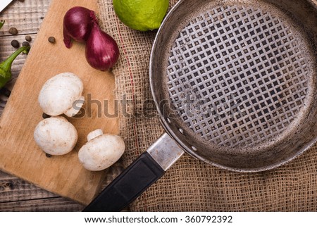 Closeup photo of empty round pan on burlap fresh champignons purple onions lime on cutting board and black pepper on wooden table, horizontal picture