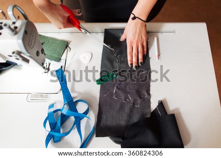 pattern, scissors, tape measure, and a sewing machine. Workplace of seamstress. Dressmaker cuts dress detail on the sketch lines.