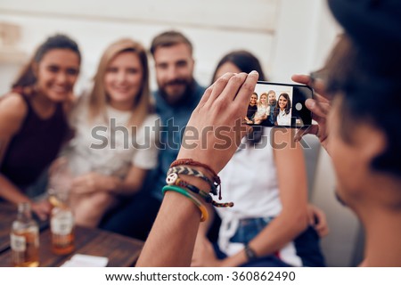 Man taking photograph of his friends with mobile phone. Young people sitting together enjoying at a party.