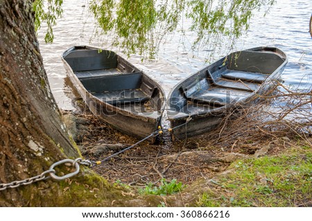 Two wooden rowing boats tied to tree on river bank