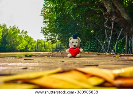 Teddy Bear and camera with red heart sitting on  the wood bridge near river - vintage tone