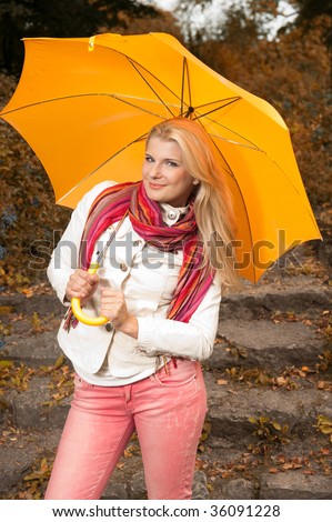 Picture of a happy pretty woman enjoing a long walk in the autumn park under the orange umbrella