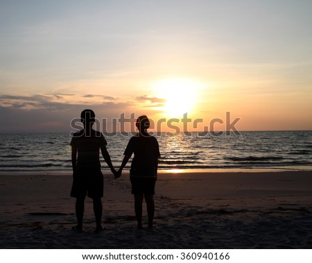 Men and women stand hand in hand to watch the sunset .