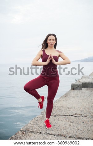 Yoga of young female near the sea. Girl standing in a Tree pose with her back to the sea