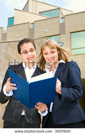 Two businesswomen are reading the documents standing outside the office building on the stairs
