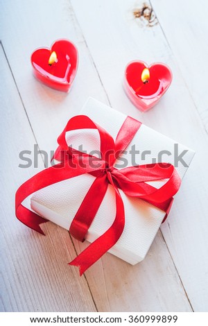 White gift box with ribbon and red candles in the shape of heart