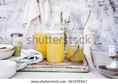 Bone broth soup in glass storage jars over  stone kitchen table. How to making base soup. 