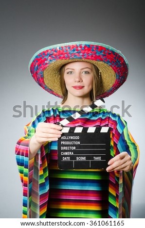 Girl in mexican vivid poncho holding clapboard against gray