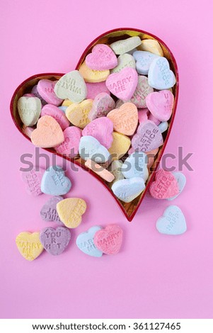 Happy Valentines Day conversation heart candy in red heart shaped gift box on pink background.