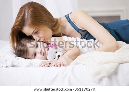 mother kissing her cute little girl on a bed