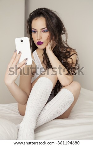 young woman with pretty makeup sitting on bed and taking selfie with her mobile phone