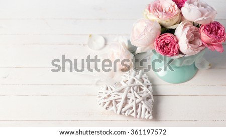 Pastel roses in turquoise vase and decorative heart on white wooden  background. Place for text. Selective focus. Toned image.