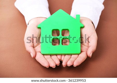 Female hands holding house on brown background