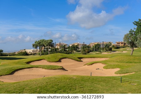 Golf course with sand trap on the background of country villas, blue sky and trees