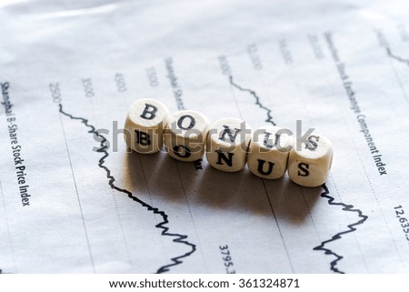 Wooden blocks with the text, BONUS, on stock charts of newspaper