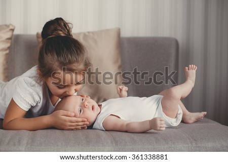 Little sister hugging her newborn brother. Toddler kid meeting new sibling. Cute girl and new born baby boy relax in a white bedroom. Family with children at home. Love, trust and tenderness Royalty-Free Stock Photo #361338881