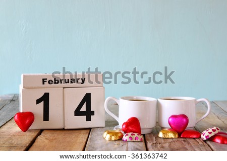 February 14th wooden vintage calendar with colorful heart shape chocolates next to couple cups on wooden table. selective focus. vintage filtered

