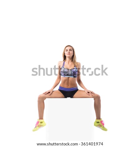 Young positive fitness woman sitting on white cube