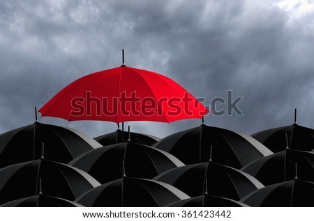 Red umbrella in mass of black umbrellas.