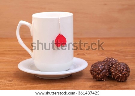 Cup of tea with heart shape on wooden table, cup standing on saucer, beside cup is sweets. Valentine's Day