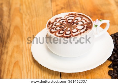 Milk foam coffee with flower pattern in a white cup on wooden background