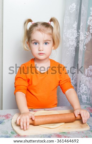 Little girl making dough in the kitchen with a rolling pin.