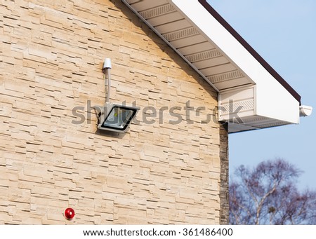 LED floodlight on wall of house covered with lite brown decorative slate stone surface.  Royalty-Free Stock Photo #361486400
