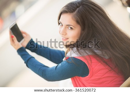 Beautiful young girl with smartphone outdoors, smiling woman taking selfie on phone, pretty female with mobile phone at city street, instagam filter like soft grain and tonality, series