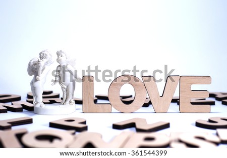 The word LOVE made of wooden letters, with a stone statuette of angels.