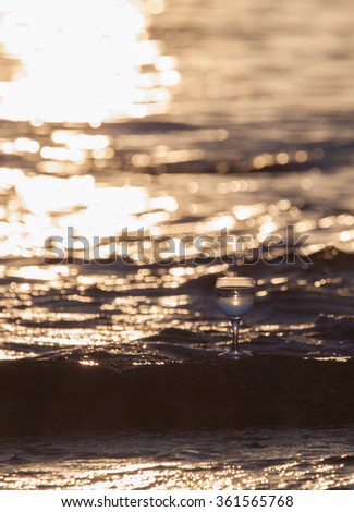 Glass of white vine with reflections of sun and sea on the background of beautiful sunset. Selective focus.
