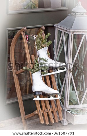 Christmas Decoration. White figure skates, old wooden sled, Christmas lantern with burning candles  near the door of the house, with vignetting