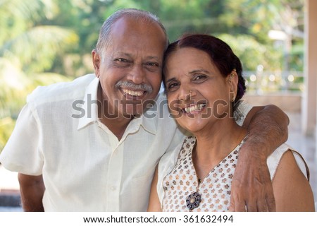 Closeup portrait, retired couple in white shirt and dress holding each other smiling,enjoying life together, isolated outside green trees background. Royalty-Free Stock Photo #361632494