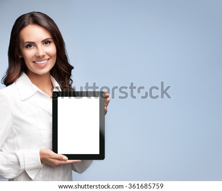 Portrait of beautiful young businesswoman showing blank no-name tablet pc monitor, over grey background, with copyspace area for slogan or text message