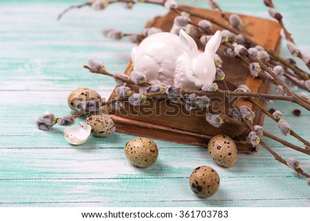 Quail eggs, decorative Easter bunny, old book and willow  branches on turquoise wooden background. Easter background. 
