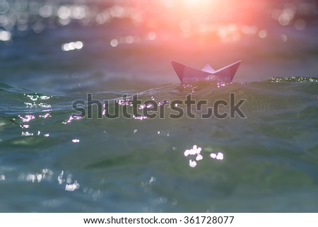 Photo closeup with sun spot one white paper origami boat riding on blue salt sea waves ocean water surface with ripples on blurred seascape background, horizontal picture 